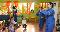 Adults performing for seated children in a colorful classroom with bright orange curtains.